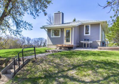 A quaint small house featuring a deck, surrounded by a lush green tree, creating a serene outdoor atmosphere.